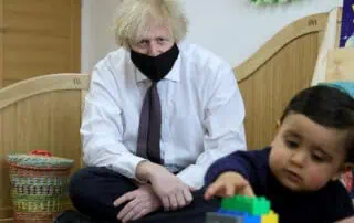 Focused adult wearing a black face mask sitting with young child in a daycare classroom, engaging in play and learning activities at Monkey Puzzle Day Nurseries.