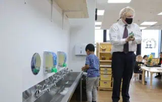 Colorful hand sanitizers and children washing hands in a bright, modern preschool classroom at Monkey Puzzle Day Nurseries. Engaging early childhood education and hygiene practices in a safe learning environment.