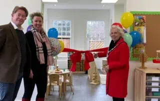 Colorful classroom celebration at Monkey Puzzle Day Nurseries during opening event, featuring teachers, staff, and children with balloons, toys, and cheerful decor.