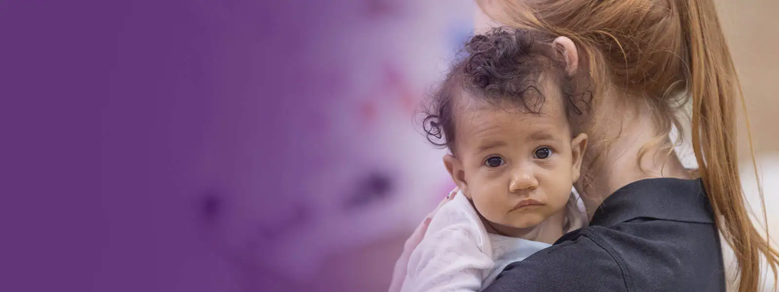 Bright-eyed toddler being comforted by a caregiver at Monkey Puzzle Day Nurseries, showcasing nurturing childcare, early childhood education, and a caring learning environment.