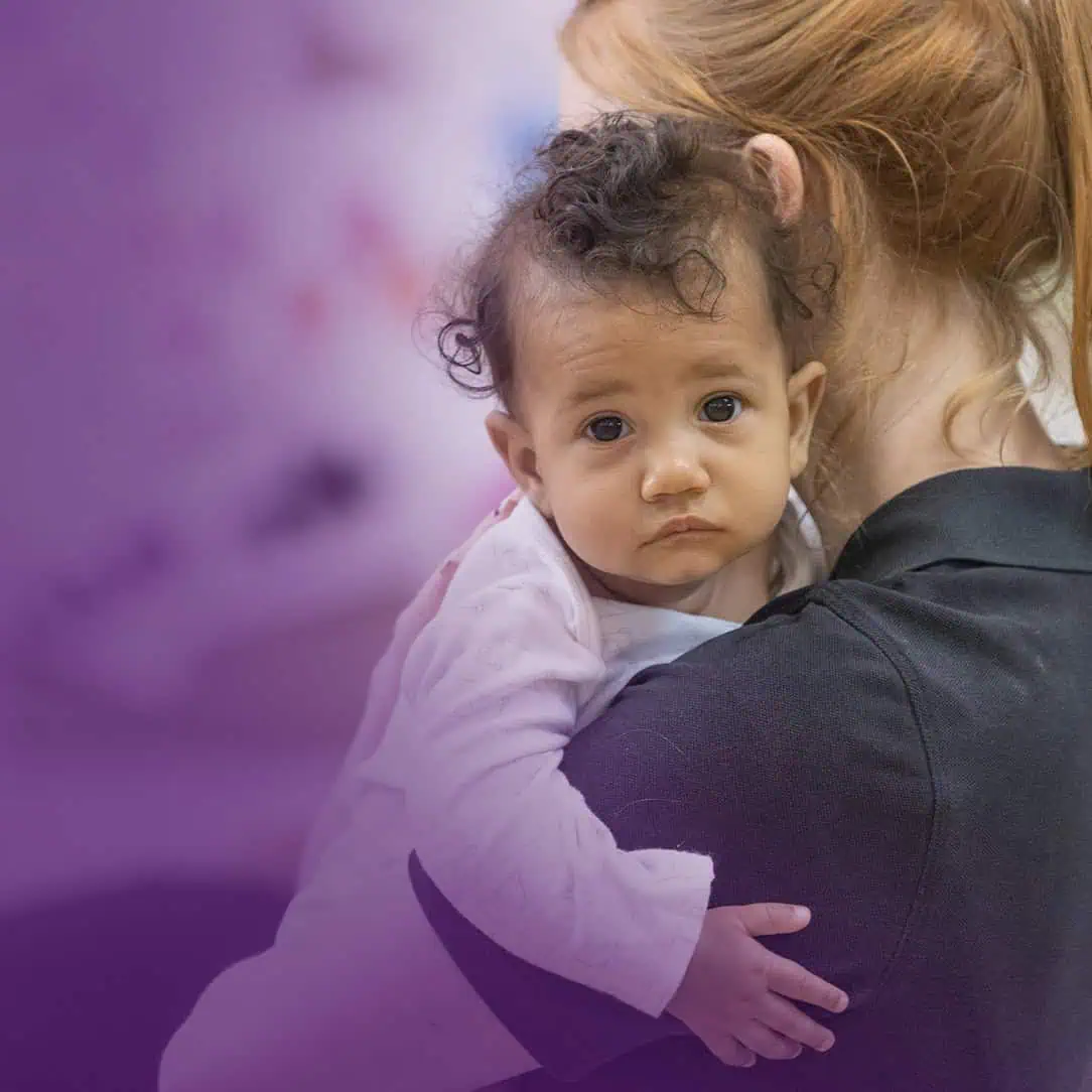 Friendly baby being held by caregiver at Monkey Puzzle Day Nurseries, emphasizing nurturing childcare and early childhood education programs.