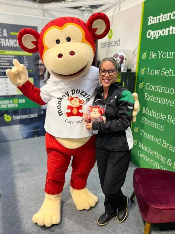 Monkey Puzzle Day Nurseries mascot with a woman at an event, promoting early childhood education and care services.