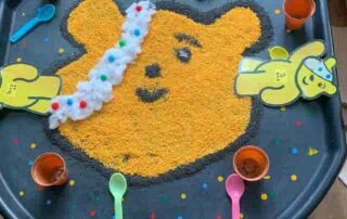 Yellow bear craft activity with colorful sand and cotton balls for toddlers at Monkey Puzzle Day Nurseries. Engaging preschool fun to develop fine motor skills and creativity.