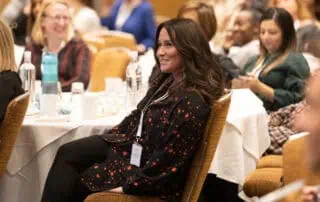Franchisees at the network Conference Professional woman smiling at a conference, sitting among engaged attendees, illustrating a positive and collaborative environment at Monkey Puzzle Day Nurseries events.
