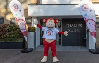 Marvin at the Network Conference Colorful monkey mascot outside Monkey Puzzle Day Nurseries, welcoming children and parents to the childcare center with branded flags, bright signage, and a friendly, engaging atmosphere.