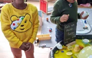 Bright-eyed African American girl smiling at the camera in a colorful daycare setting at Monkey Puzzle Day Nurseries, highlighting early childhood education and vibrant learning environments.