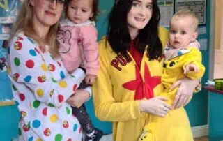 Smiling woman with children in colorful costumes at Monkey Puzzle Day Nurseries, showcasing happy staff and children engagement in playful activities.