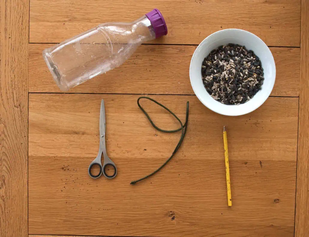 Colorful plastic bottle, sunflower seeds, scissors, elastic band, and ruler on wooden table at Monkey Puzzle Day Nurseries for creative and sensory activities.