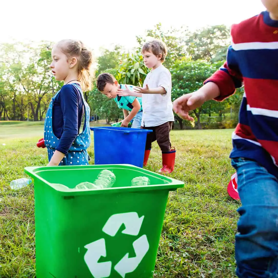 Recycle activity with children at outdoor day nursery, environmental learning for preschoolers, kids sorting plastic bottles into recycling bins for eco-awareness, early childhood education, outdoor play.