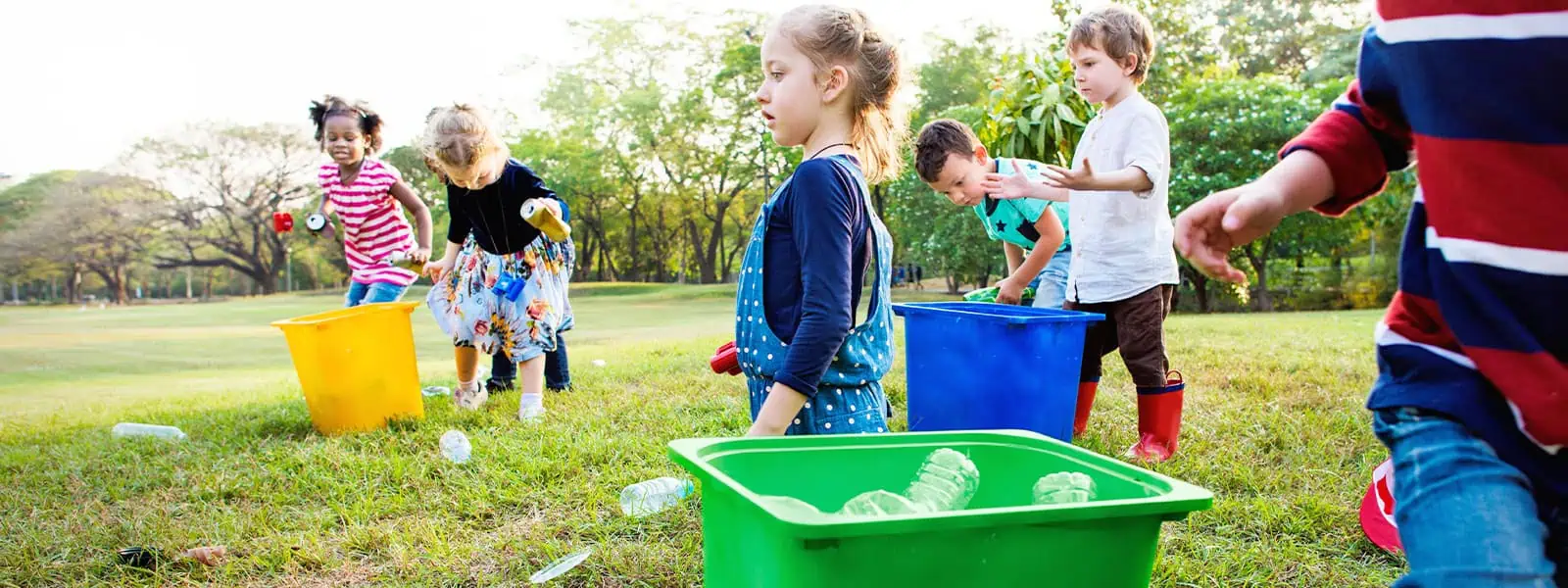 Colorful children playing outdoors with trash bins and plastic bottles at Monkey Puzzle Day Nurseries, promoting environmental awareness and fun activities for early childhood education.