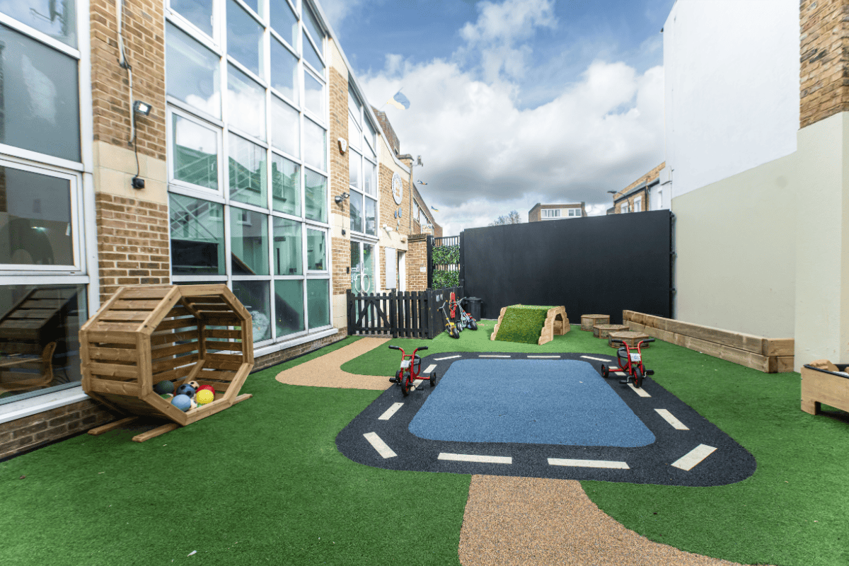 A vibrant outdoor play area at Monkey Puzzle Olympia nursery featuring soft artificial grass, a mini road with a bike track, and engaging play structures for young children.