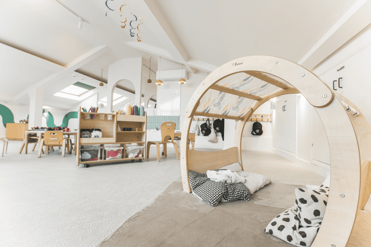 A cozy play area featuring a wooden semi-circular climbing frame with cushions and soft mats, designed for young children’s comfort and development.