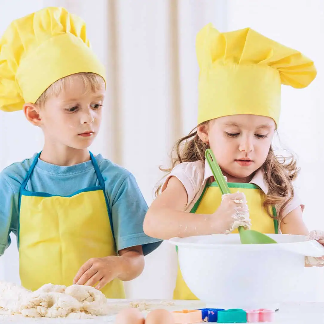 Children baking with yellow chef hats and aprons at Monkey Puzzle Day Nurseries, engaging in fun and educational cooking activities for early childhood development.