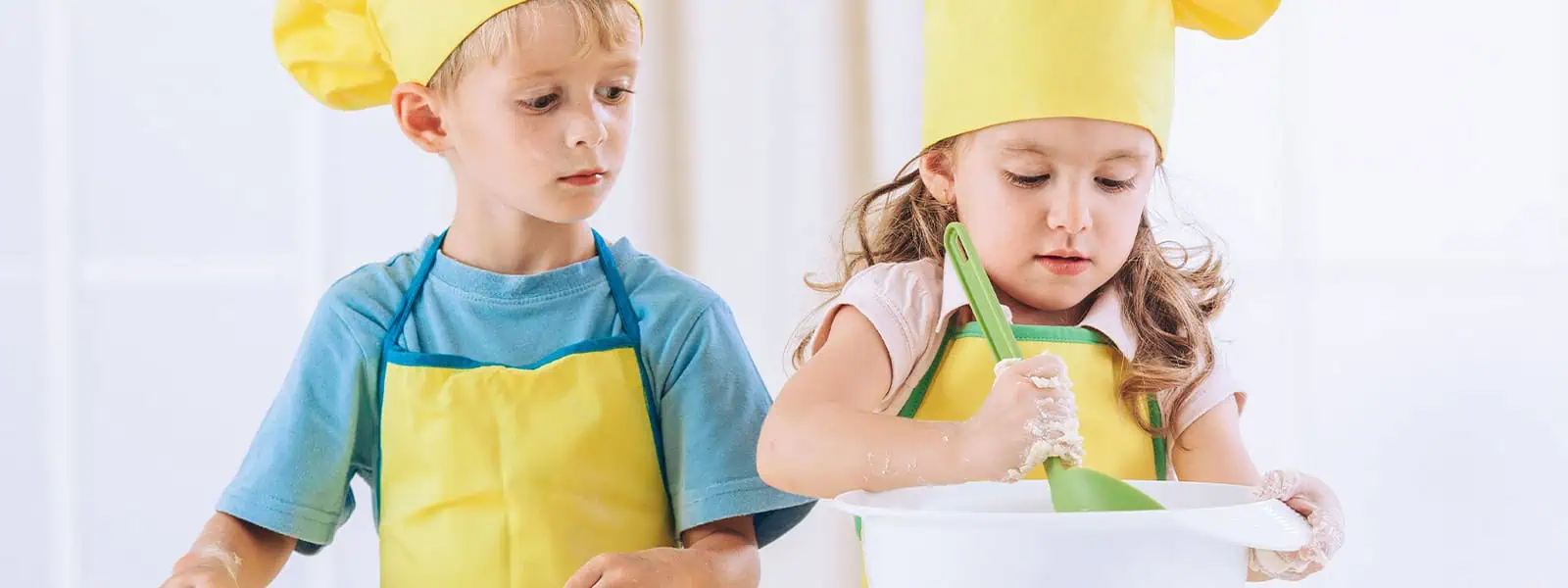Children cooking or baking in a nursery, wearing yellow aprons and chef hats for a cooking activity at Monkey Puzzle Day Nurseries.