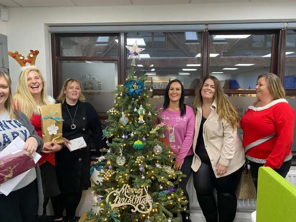 Christmas team celebration at Monkey Puzzle Day Nurseries with staff in festive attire around a decorated Christmas tree.