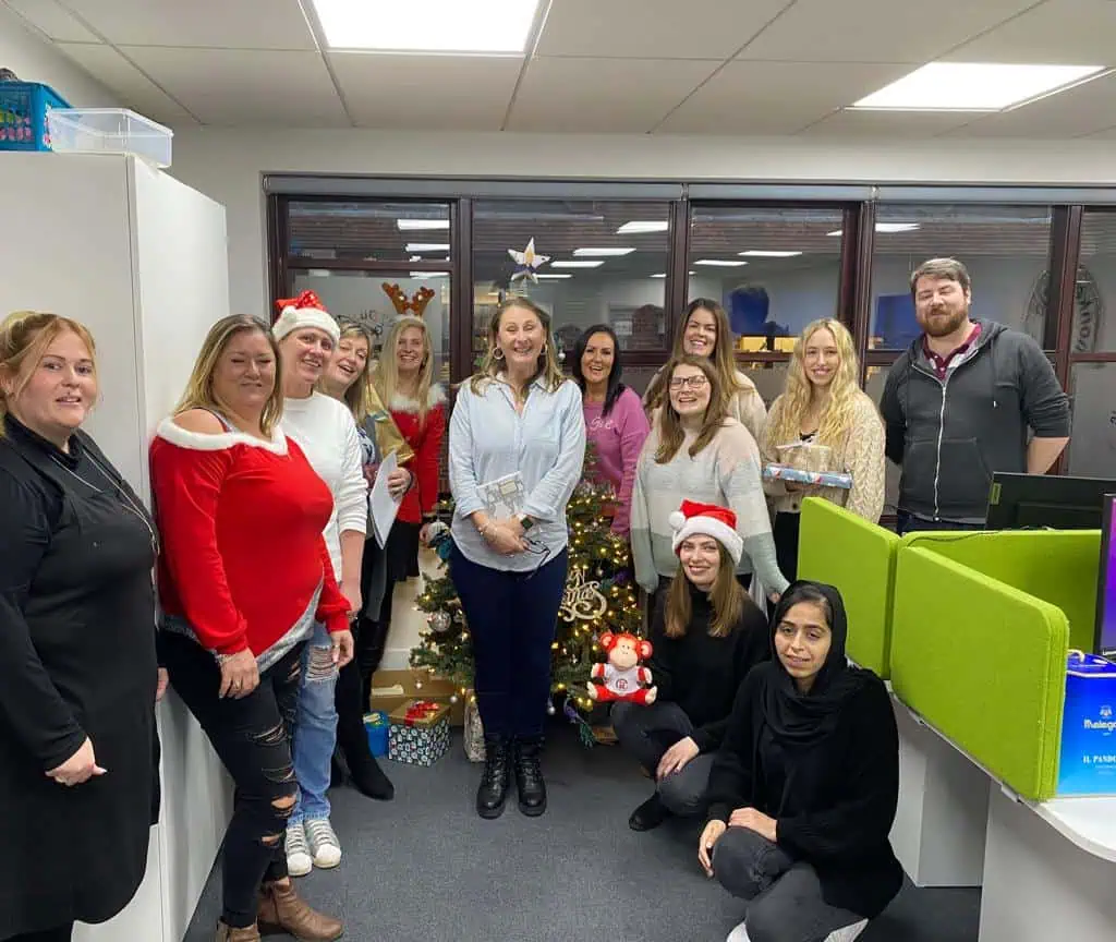 Christmas office celebration at Monkey Puzzle Day Nurseries with staff in festive attire around a decorated Christmas tree and gift presents.