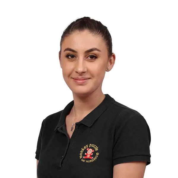 Friendly female staff member wearing a Monkey Puzzle Day Nurseries uniform, representing caring childcare professionals at the trusted nursery.