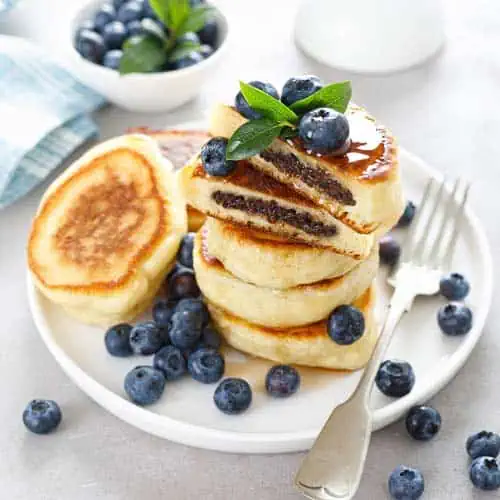 Fresh fluffy blueberry pancakes stacked with blueberries and garnished with mint on a white plate, ideal for breakfast or brunch at Monkey Puzzle Day Nurseries.