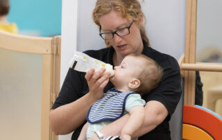 Monkey Puzzle Nursery Practitioner bottle feeding a baby during meal time