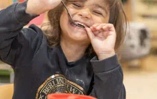 Child enjoying mealtime at Monkey Puzzle Day Nurseries, happy kid with food, playful eating experience, early childhood development, caring nursery environment.