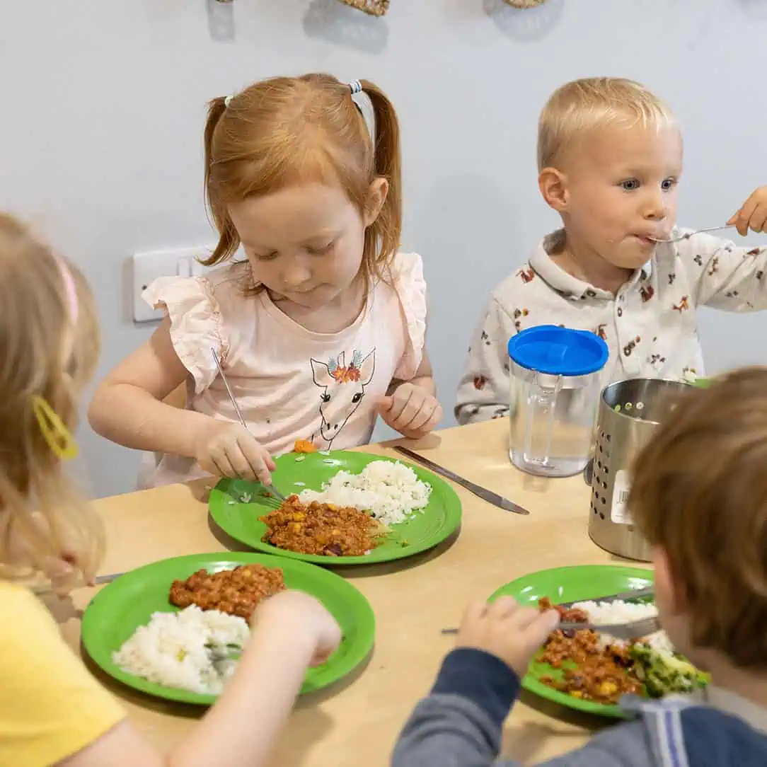 Tiny children eating healthy food at daycare, toddler meal time in day nursery, young kids enjoying lunch together in preschool setting, happy preschoolers eating in a childcare environment, relevance: high for child care and preschool SEO.