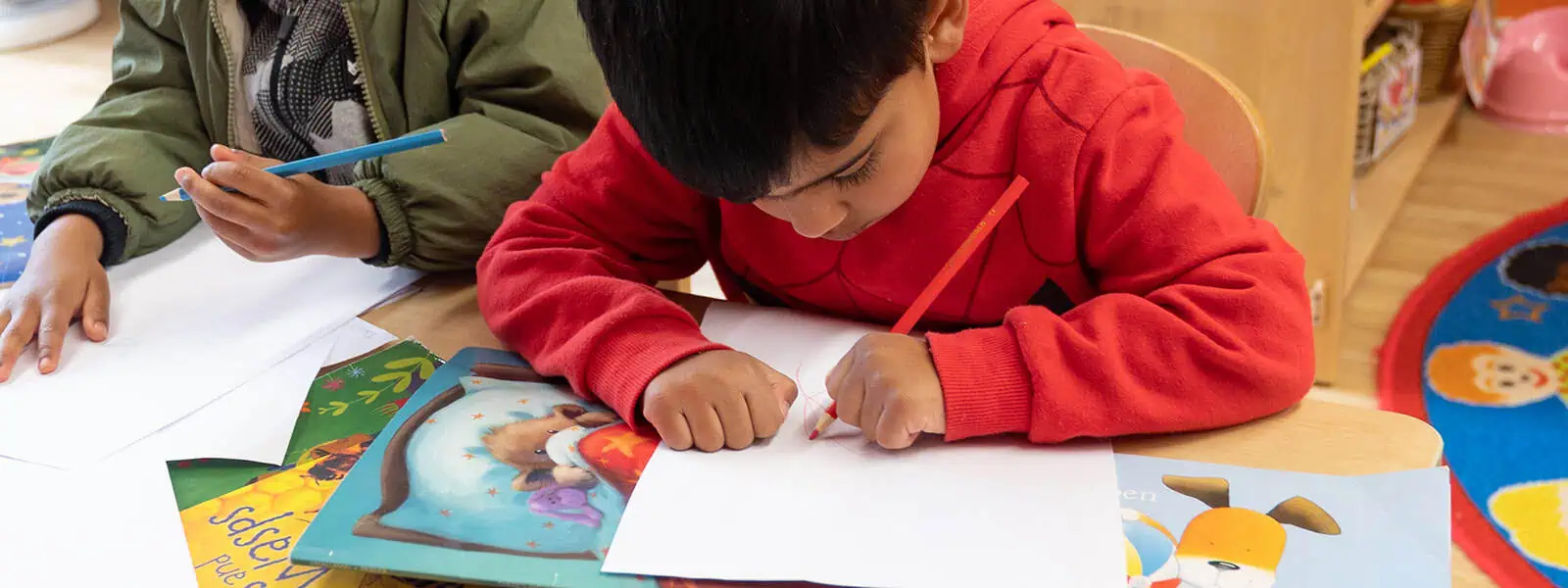 Bright young children engaged in drawing and reading activities at Monkey Puzzle Day Nurseries, fostering early childhood education and learning through play.