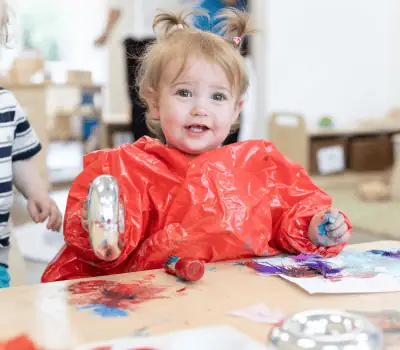 Bright young child engaging in creative painting activity at Monkey Puzzle Day Nurseries with colorful art supplies in a friendly preschool environment.
