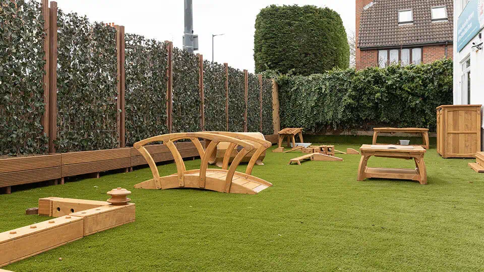 Children's outdoor wooden play area at Monkey Puzzle Day Nurseries with soft artificial grass and various play structures.