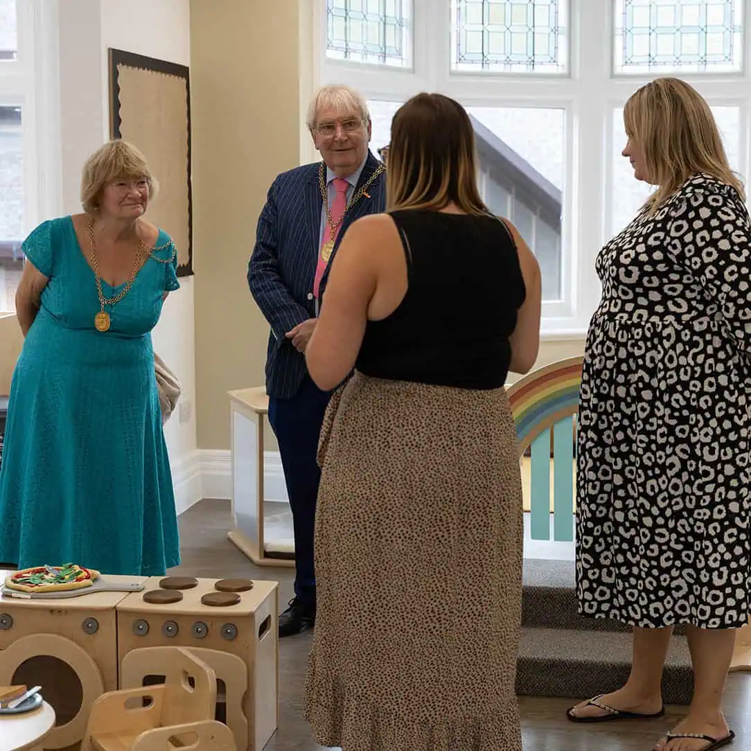 Mayor Dennis Booth at Monkey Puzzle Guildford Celebration at Monkey Puzzle Day Nurseries with staff and community members dressed in colorful attire, engaging in a joyful event within the nursery environment.