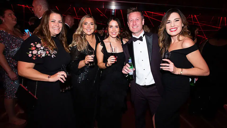 Celebration event at Monkey Puzzle Day Nurseries with happy adults in formal attire, enjoying drinks and socializing in a vibrant, modern setting.