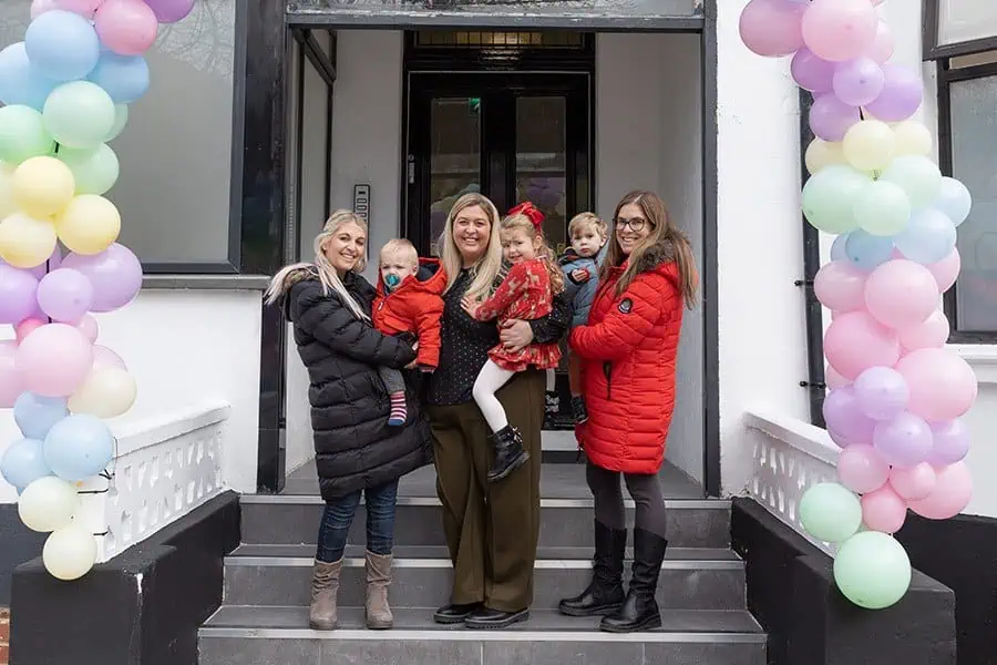 Nursery Manager Liesl meeting new families Colorful balloon arch at entrance of Monkey Puzzle Day Nurseries during grand opening with staff and children, showcasing a welcoming environment for early childhood education.