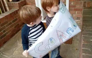 Children with banner to support Andy Giant colorful children's drawing held by two young boys outside Monkey Puzzle Day Nurseries.