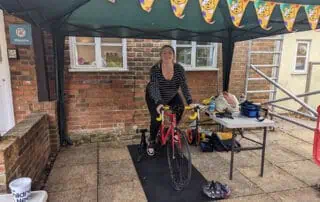 Staff helping to raise money for charity A woman riding a stationary bike under a canopy at Monkey Puzzle Day Nurseries, surrounded by outdoor play and activities for early childhood development.