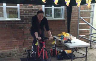 Staff supporting Andy, taking turns on the bike Bike riding outdoor activity at Monkey Puzzle Day Nurseries, children enjoying fun and engaging outdoor playtime with biking equipment and festive decorations.