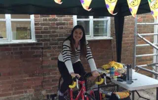 Staff team doing their part on the sponsored bike ride Cyclist woman smiling under colorful bear-themed pennant banner at Monkey Puzzle Day Nurseries.