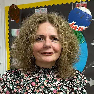 Bright smiling woman with curly hair in a colorful classroom at Monkey Puzzle Day Nurseries, showcasing a welcoming environment for early childhood education.