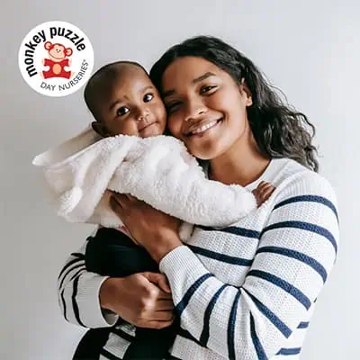 Bright young caregiver holding a happy toddler at Monkey Puzzle Day Nurseries, emphasizing caring childcare and early childhood education services.