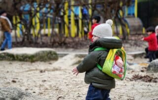 Brightly dressed young children playing outdoors at Monkey Puzzle Day Nurseries, exploring nature and engaging in age-appropriate activities in a safe, educational environment.