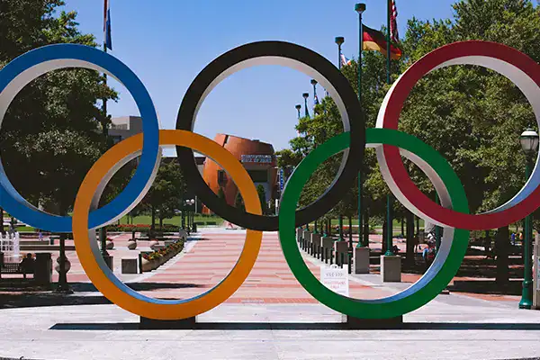 Colorful Olympic rings in a park, symbolizing unity and diversity, with a backdrop of trees and clear sky. Ideal for highlighting community, sports, and recreational activities in a family-friendly environment.