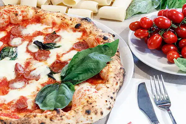 Freshly baked pepperoni pizza with basil leaves on top, served at Monkey Puzzle Day Nurseries family dining area.