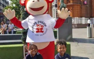 Monkey puzzle day nursery mascot in city square with happy children, promoting early childhood education and fun activities at Monkey Puzzle Day Nurseries.