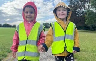 Kids wearing high visibility vests walking hand in hand outdoors at Monkey Puzzle Day Nurseries, early childhood development, outdoor play, preschool activities, children in safety gear for outdoor adventure.