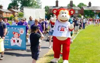 Colorful event at Monkey Puzzle Day Nurseries featuring children and families enjoying outdoor activities with the nursery mascot mascot on a sunny day.