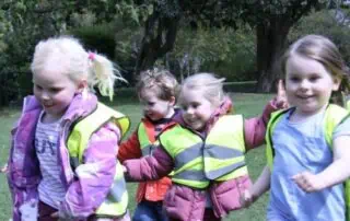 Children in high-visibility jackets playing outdoors at Monkey Puzzle Day Nurseries, emphasizing early childhood education and outdoor activities.