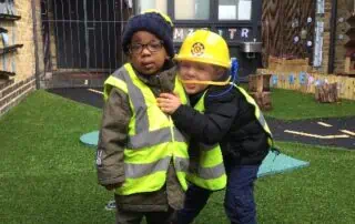 Bright young children dressed in safety gear playing outside at Monkey Puzzle Day Nurseries, emphasizing early childhood development and outdoor learning environments.