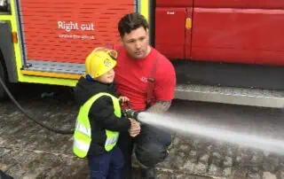 Child and firefighter practicing fire safety at Monkey Puzzle Day Nurseries, emphasizing early fire awareness and emergency response training for young children.