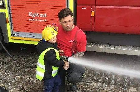 Fireman showing off fire service equipment with children Child and firefighter practicing fire safety at Monkey Puzzle Day Nurseries, emphasizing early fire awareness and emergency response training for young children.