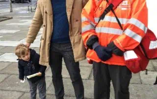 Friendly crossing guard greeting children and parents near Monkey Puzzle Day Nurseries, ensuring safety for young kids in an urban environment.