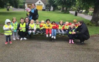 Brightly dressed young children at a Monkey Puzzle Day Nursery outdoor activity, wearing high-visibility vests, engaging in social and learning experiences in a safe, welcoming environment.