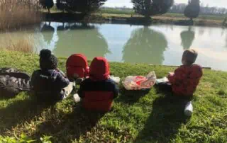 Children sitting by a pond at Monkey Puzzle Day Nurseries, enjoying outdoor learning and nature exploration activities.